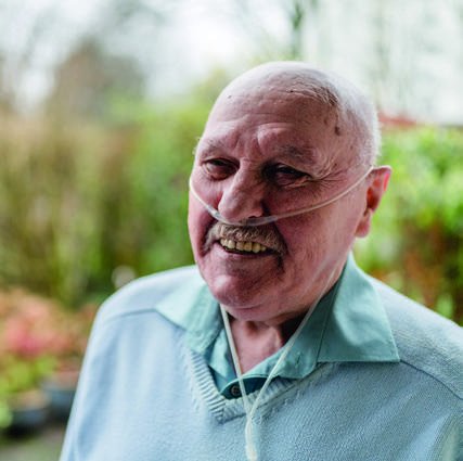 Porträt von Rainer, 78 Jahre, der seit Jahren mit COPD lebt, im Freien vor grünem Hintergrund.